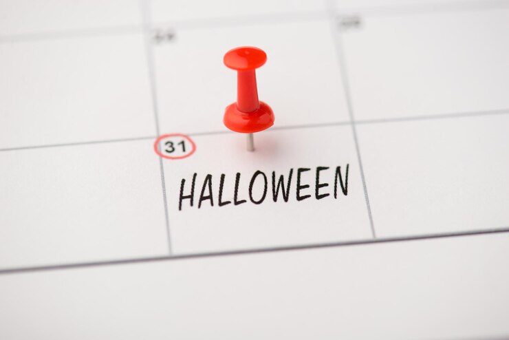Zdjęcie powyżej zdjęcie etykiety z datą 31 października napisem halloween i czerwoną szpilką na białym tle na tle kalendarza