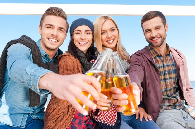 Pozdrawiam! Grupa młodych, szczęśliwych ludzi dopingujących piwem i uśmiechających się, łącząc się ze sobą