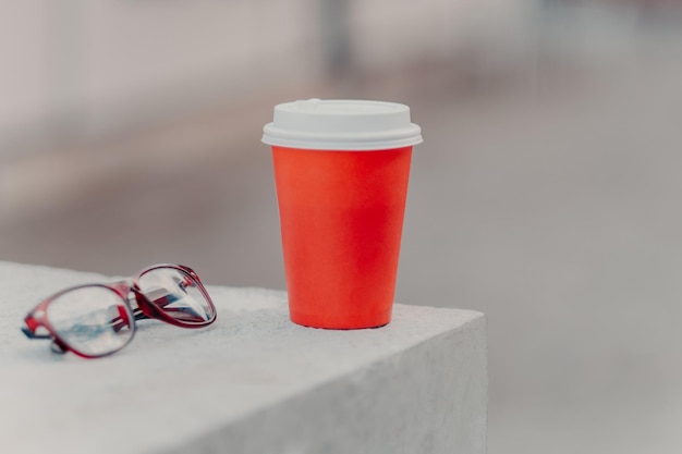 Poziome ujęcie czerwonej kawy na wynos i okulary optyczne Aromatyczna kawa do picia Koncepcja picia Papierowy kubek gorącego napoju