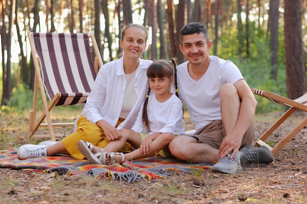 Poziome Ujęcie Rodziny W Białych Koszulach Siedzącej Na Kocu W Parku I Patrzącej Na Kamerę Z Uśmiechem Kaukascy Rodzice Z Małą Córką Relaks W Lesie Razem