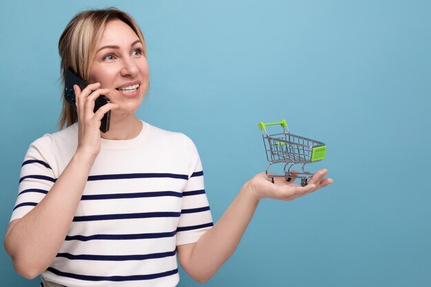 Poziome zdjęcie na baner atrakcyjnej kupującej dziewczyny rozmawiającej przez telefon trzymającej wózek na zakupy