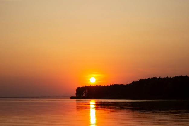 Zdjęcie poziome zdjęcie złotego zachodu słońca nad rzeką lub morzem. odbicie w wodzie jak ogień. wybrzeże.