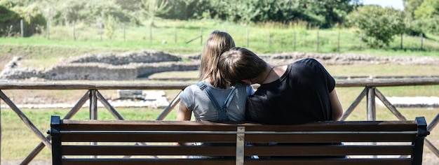 Poziomy baner lub nagłówek z widokiem z tyłu młodej pary Gen Z siedzącej na ławce w parku kampusu