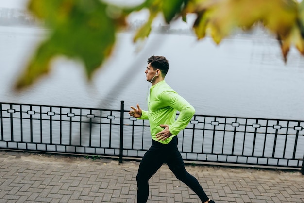 Poziomy widok z góry obraz młodego biegacza biegającego rano na tle jeziora mgła Fitness mężczyzna ćwiczenia w parku i słuchanie muzyki na słuchawkach Ludzie i koncepcja sportu