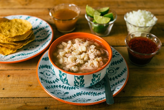 Pozole podawane w głębokim naczyniu z salsą tostadas i warzywami na drewnianym stole