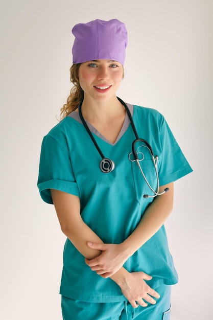 Pozytywna dama w zielonej medycznej odzieży roboczej i stetoskopie patrząca w kamerę stojąc w studio