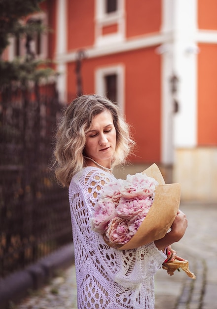 Pozytywna dziewczyna trzyma kwiaty w centrum miasta Bliska strzał niesamowite blond włosy pani z naturalnym makijażem wygląd szczęśliwy spacery na świeżym powietrzu trzymać różowy bukiet