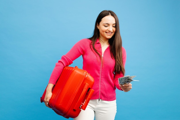Pozytywna dziewczyna z bagażem i pieniędzmi zamierza podróżować Kobieta w różowym swetrze i dżinsach stojących na niebieskim tle Koncepcja wakacji