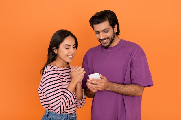 Pozytywna indyjska młoda para za pomocą telefonu komórkowego na pomarańczowo