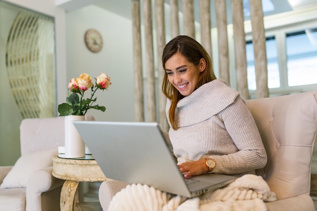 Pozytywna Młoda Kobieta Freelancer Oglądając Wideo W Blogu Na Netbooku I Wypijając Kawę W Wygodnym Domu. Piękna Młoda Biznesowa Kobieta Pracuje Na Laptopie. Freelancer łączy Się Z Internetem