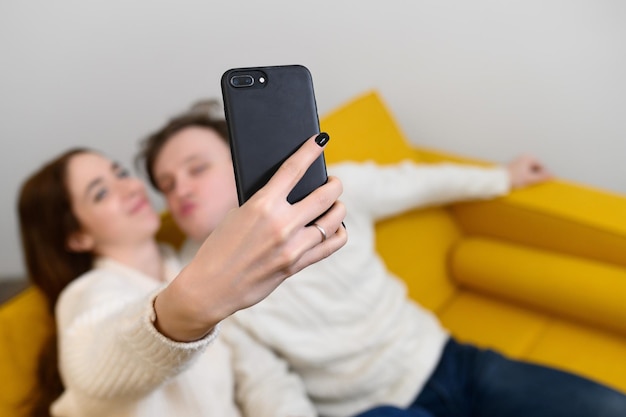 Pozytywna młoda para robi selfie siedząc na kanapie w domu wysokiej jakości zdjęcie