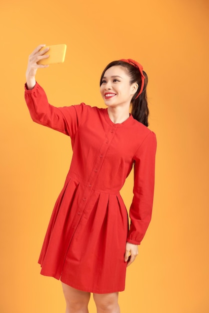 Pozytywna wesoła azjatycka kobieta biorąca selfie na żółtym tle