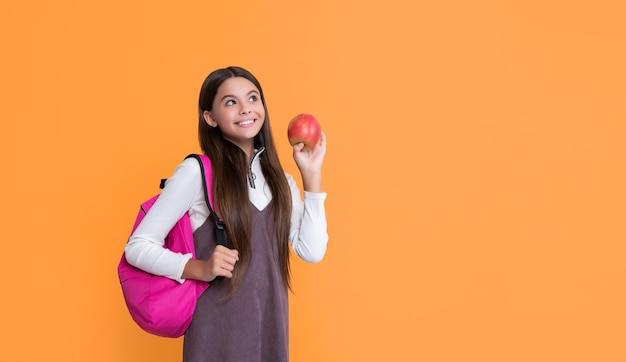 pozytywne dziecko ze szkolnym plecakiem i jabłkiem na żółtym tle