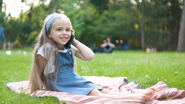 Pozytywne małe dziecko dziewczynka o rozmowę na jej telefon komórkowy w letnim parku. Młoda kobieta dziecko rozmawia sellphone.