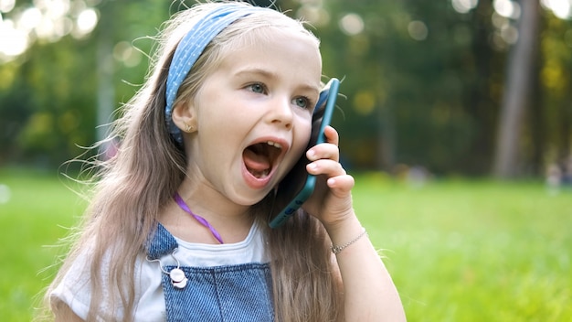 Pozytywne małe dziecko dziewczynka o rozmowę na jej telefonie komórkowym w letnim parku.