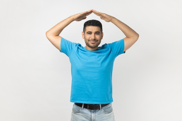 Pozytywnie uśmiechnięty mężczyzna ubrany w niebieską koszulkę stojący wykonujący gest na dachu, czujący się bezpiecznie