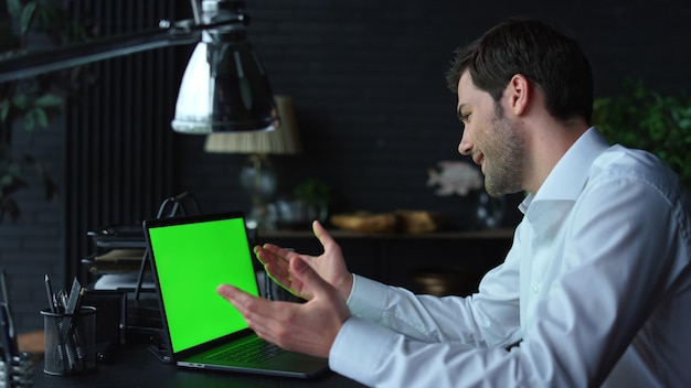 Pozytywny biznesmen wideo na czacie online na laptopie z zielonym ekranem w biurze
