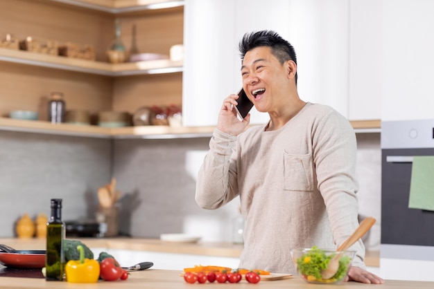 Pozytywny chiński człowiek gotuje zdrową sałatkę i rozmawia przez telefon
