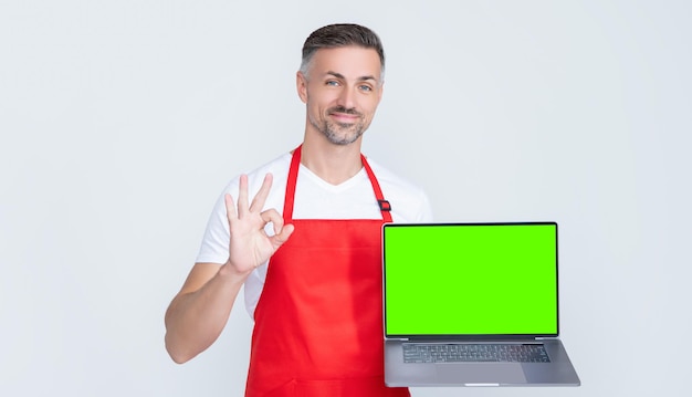 Pozytywny dojrzały mężczyzna w fartuchu przedstawiający laptopa z miejscem na kopię