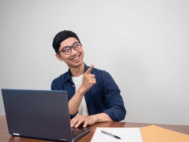 Pozytywny mężczyzna nosi okulary, wskazuje palcem i siedzi przy stole roboczym