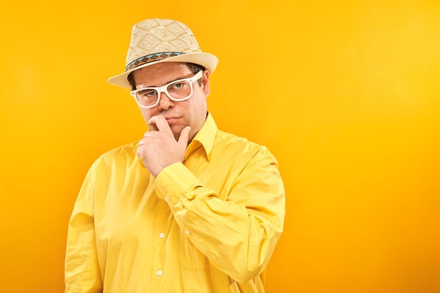 Pozytywny mężczyzna w kapeluszu panamskim trzymający podbródek myśli o wakacyjnych wątpliwościach, podejmuje decyzję odizolowaną na żółtym tle studia