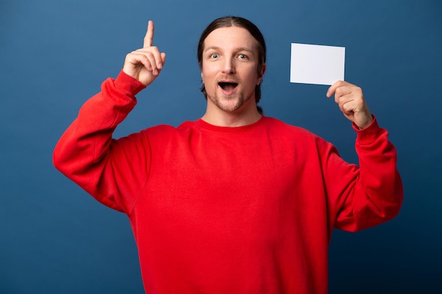 Zdjęcie pozytywny szczęśliwy facet w czerwonej koszulce zdumiony patrzy na kamerę i wskazuje palcami w górę zaskoczony wyraz twarzy stoi na odizolowanym niebieskim tle