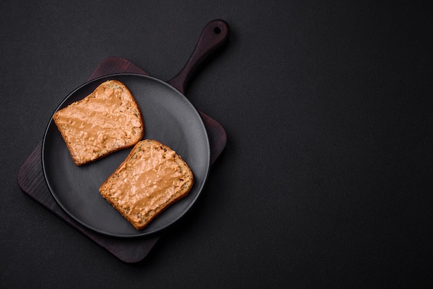 Pożywna kanapka składająca się z chleba i masła orzechowego na czarnym talerzu ceramicznym