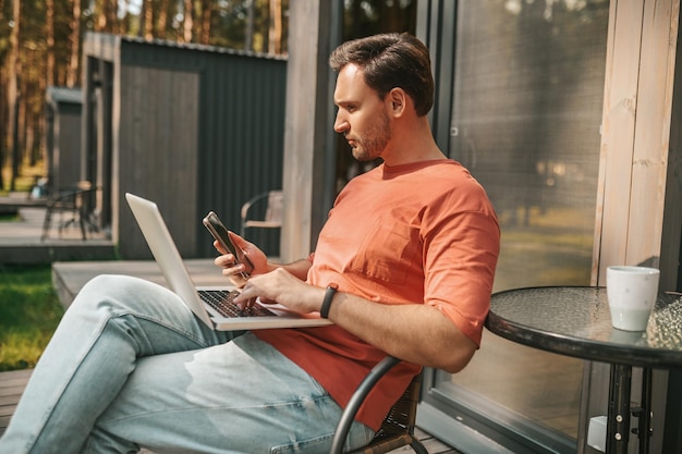 Zdjęcie praca w domu. młody mężczyzna z laptopem siedzący na zewnątrz i pracujący online