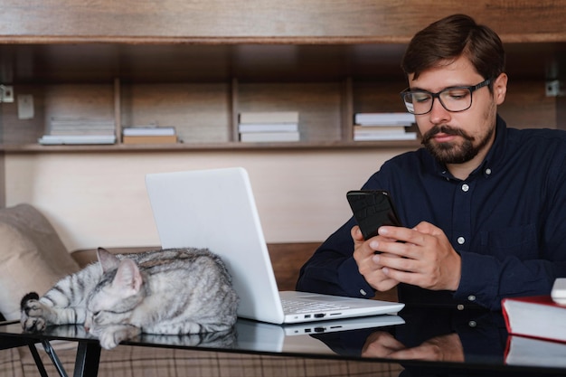 Praca w domu ze zwierzęciem leżącym na kolanach Mężczyzna pracuje w domu, pisząc na laptopie