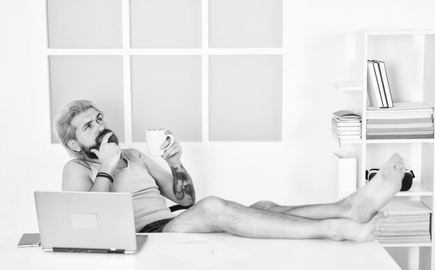 Praca z wygodą samokształcenie online zostań w domu zablokowanie koronawirusa kwarantanna odległy biznes boso biznesmen przy laptopie w domowym biurze brodaty mężczyzna myśli i pije kawę