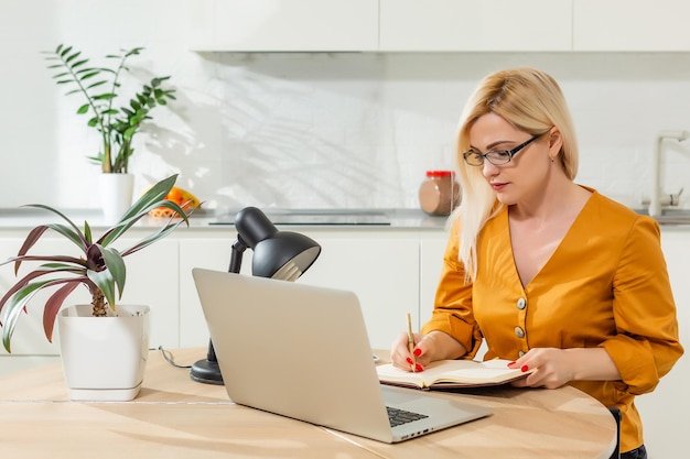 Praca zdalna z domu. Młoda kobieta za pomocą laptopa. Miejsce pracy freelancera w biurze w kuchni. Telepraca w izolacji, kobiecy biznes, zakupy online. Student w kształceniu na odległość. Moment życia.