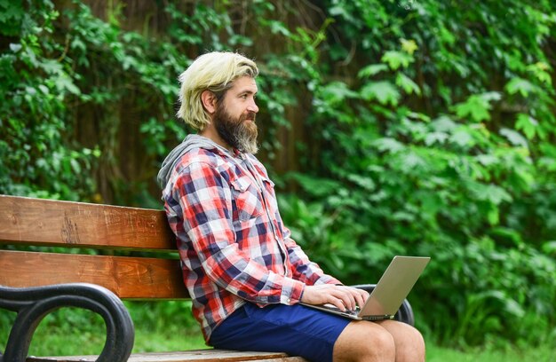 Praca zdalna Zakupy online Zwinny biznes Brodaty facet siedzi na ławce w parku Natura Tło Praca i relaks Praca online Hipsterska praca w parku Świeże powietrze Mobilny internet Nowoczesny laptop