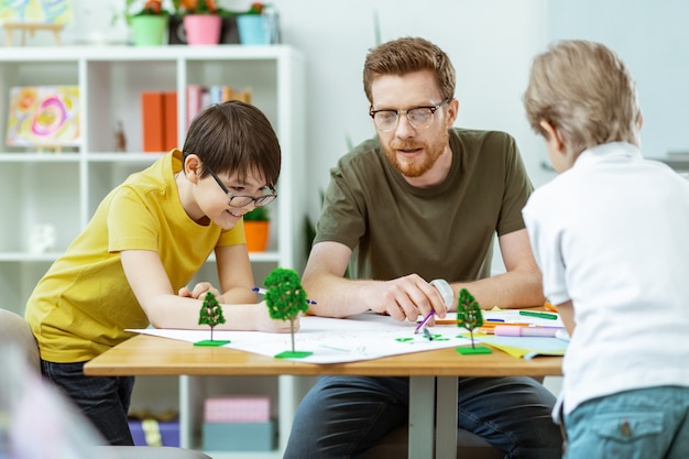 Pracowici studenci. Inteligentna nauczycielka z brodą wskazującą na obrazki i wyjaśniająca młodym miłośnikom przyrody znaczenie meaning