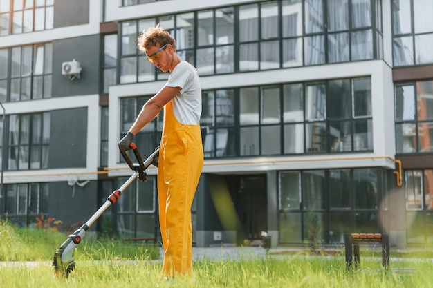 Zdjęcie pracowity dzień mężczyzna kosi trawę kosiarką na zewnątrz na podwórku