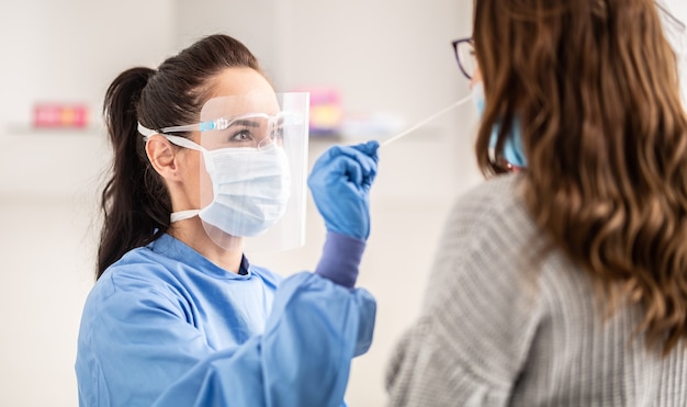 Pracownica personelu medycznego nosząca sprzęt ochronny pobiera próbkę z nosa pacjenta do testu antygenowego na obecność koronawirusa.
