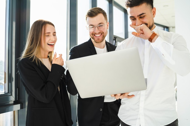 Pracownicy biura śmieją się patrząc na laptopa