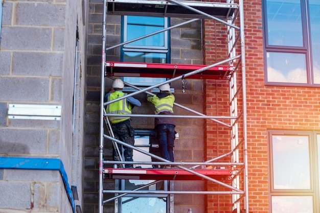 Pracownicy budowlani wykorzystujący aluminiową mobilną wieżę rusztowania i szelki bezpieczeństwa do pracy na wysokości