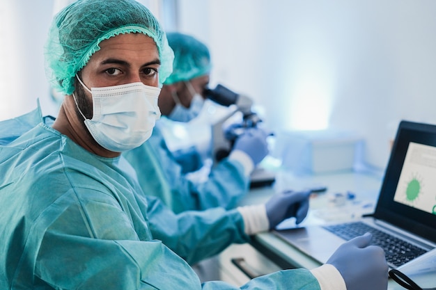 Pracownicy Medyczni W Kombinezonach Ochronnych Pracujący Z Laptopem W Laboratorium Szpitalnym Podczas Epidemii Koronawirusa - Skoncentruj Się Na Lewej Twarzy Lekarza