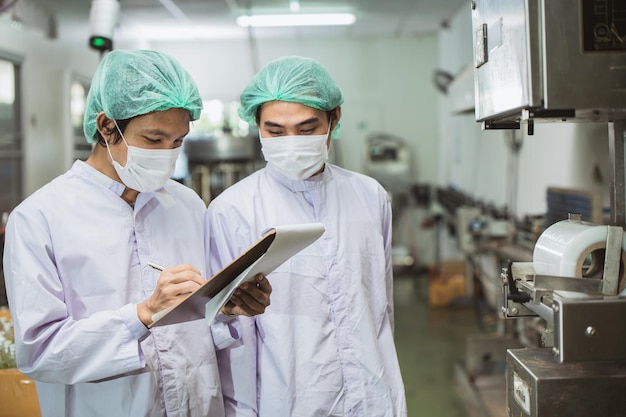 Pracownicy płci męskiej pracujący razem w fabryce napojów napojów z higienicznym pracownikiem bezpieczeństwa sprawdzają proces jakości produktu