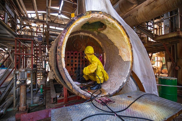Pracownicy płci męskiej używają strumieni wody pod wysokim ciśnieniem do czyszczenia brudu kotłów rurowych w obszarach przemysłowych lub toksycznego materiału niebezpiecznego siarki