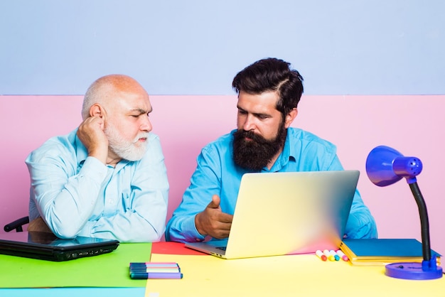 Pracownicy siedzą przy biurku patrzą na ekran laptopa współpracując w biurze Biznesmen czyta wiadomości w Internecie Dwóch kolegów pracujących razem w biurze na kolorowym tle