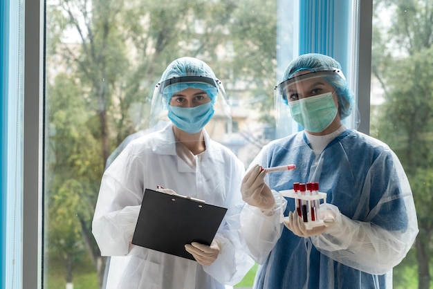 Pracownicy służby zdrowia w masce ochronnej, osłonie twarzy i rękawiczkach piszą rezult pacjenta testowego na koronawirusa