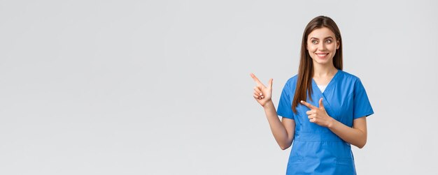 Pracownicy służby zdrowia zapobiegają koncepcji ubezpieczenia i medycyny wirusowej Uśmiechnięta ładna pielęgniarka lub lekarz w niebieskich zaroślach wskazujących palce w lewo i patrzących na baner z zadowolonym uśmiechem na szarym tle