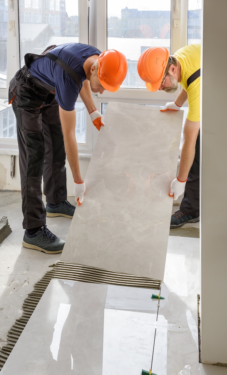 Zdjęcie pracownicy układają na podłodze dużą płytkę ceramiczną
