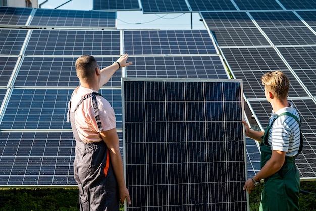 Pracownicy w mundurze ochronnym niosący panel słoneczny do instalacji na nowej stacji, zielona energia