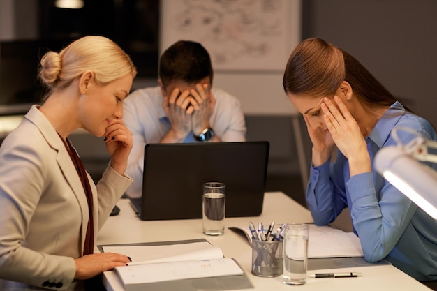 Zdjęcie pracownicy z laptopem i dokumentami pracujący późno w nocy w biurze