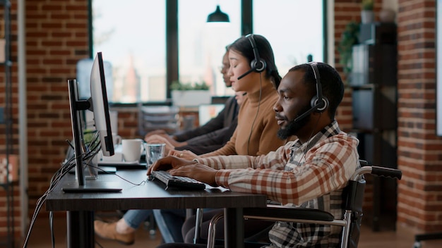 Zdjęcie pracownik afroamerykanin używający słuchawek do rozmów z klientami, pomagający w sprzedaży i udzielający pomocy telemarketingowej w call center. mężczyzna rozmawiający z osobami w biurze przyjaznym niepełnosprawnym.