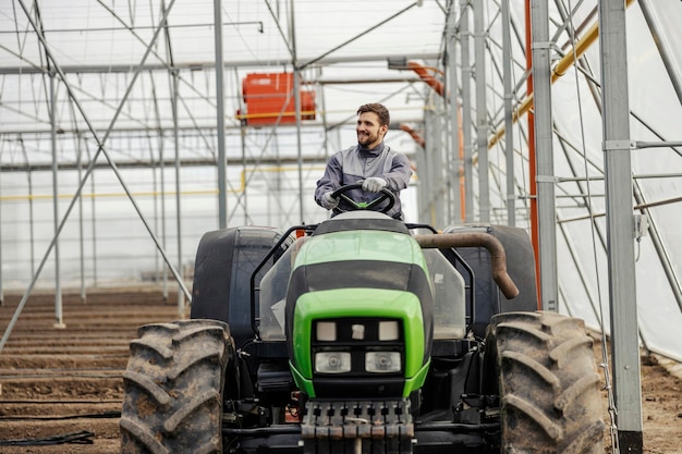 Zdjęcie pracownik agronomii orze ziemię ciągnikiem w szklarni