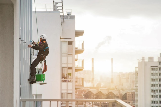 Pracownik alpinizmu przemysłowego w mundurze wisi nad budynkiem elewacji mieszkalnej mycie przeszkleń zewnętrznych