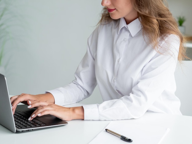 Pracownik biurowy Elegancka kobieta Połączenie online Nie do poznania uśmiechnięta dama w białej koszuli pisząca laptopa siedzącego na biurku w jasnym wnętrzu pokoju
